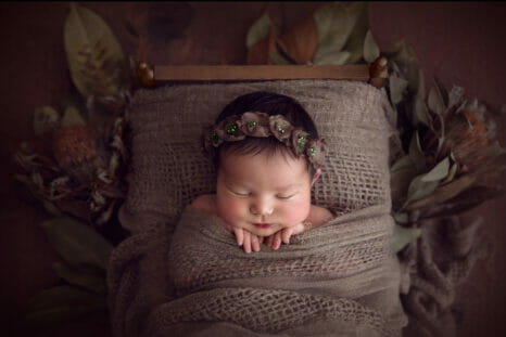 newborn baby tucked into a bed while wearing a headband by Kelly Brown Photography workshop UK